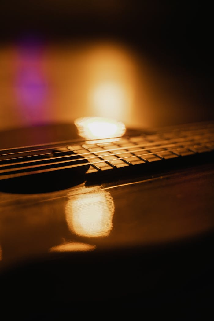 Moody close-up of an acoustic guitar with warm lighting and reflections.